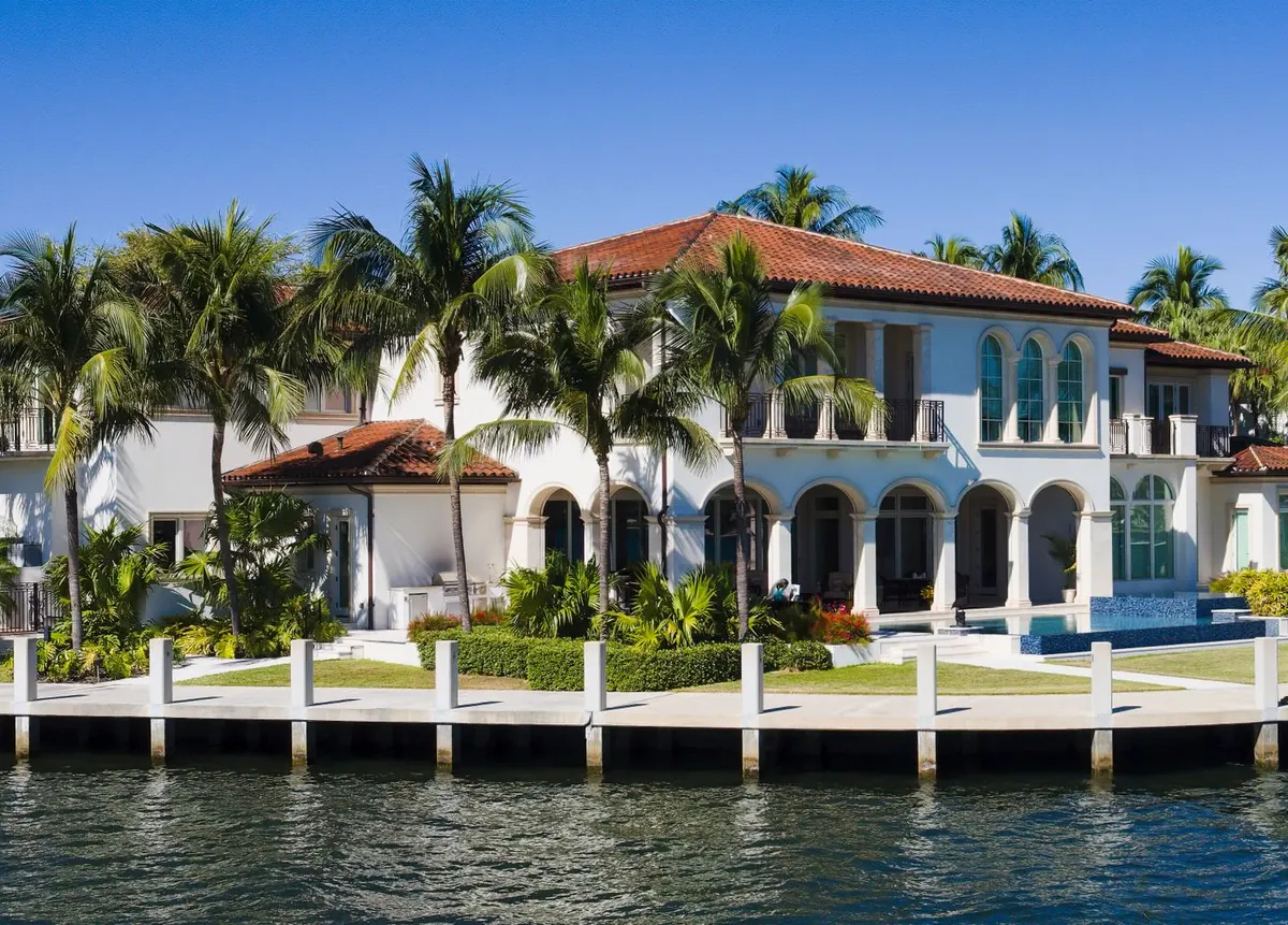 White stucco Fort Lauderdale home with arched windows, palms and a canal seawall